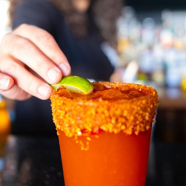 A bartender garnishes a michelada with a lime wedge at The Last Round Tavern.