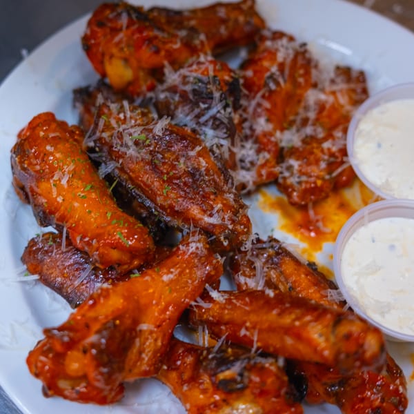 A plate of buffalo wings from The Last Round Tavern, topped with parmesan cheese and two dipping sauces.