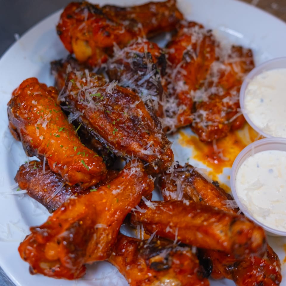 A plate of buffalo wings from The Last Round Tavern, topped with parmesan cheese and two dipping sauces.
