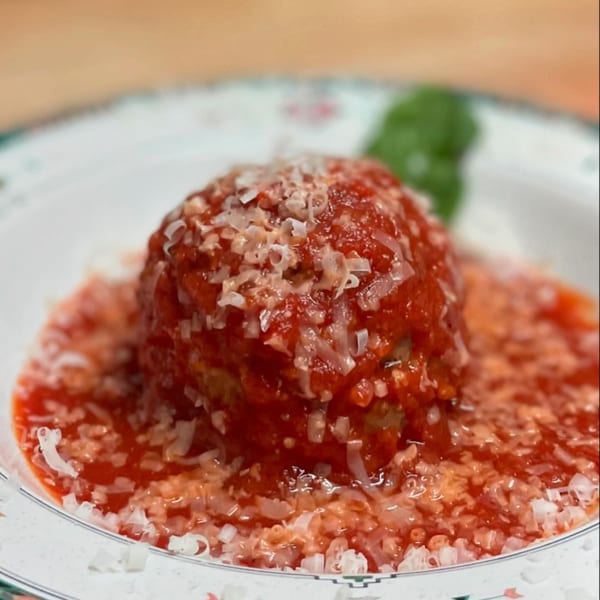 A large meatball covered in red sauce and grated cheese, with a basil leaf in the background.