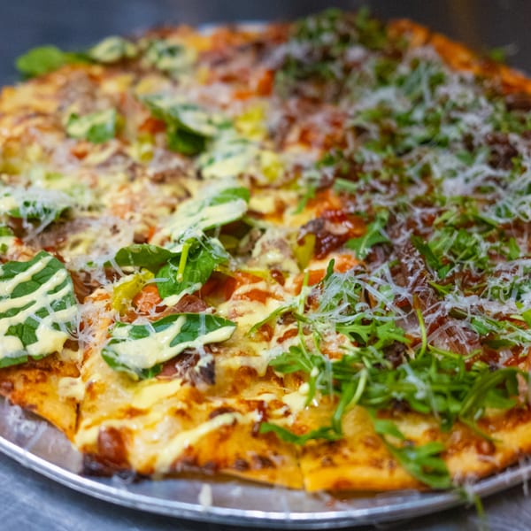 A large pizza from The Last Round Tavern, half topped with spinach and sauce, half with arugula.