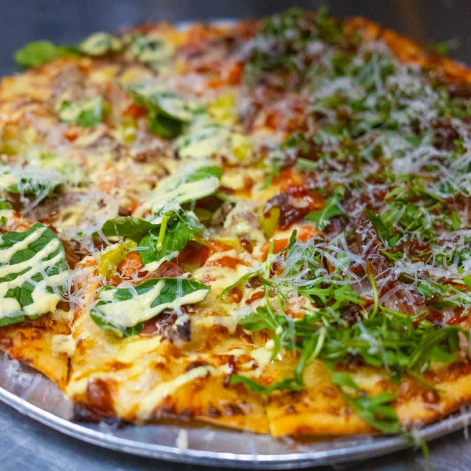 A large pizza from The Last Round Tavern, half topped with spinach and sauce, half with arugula.