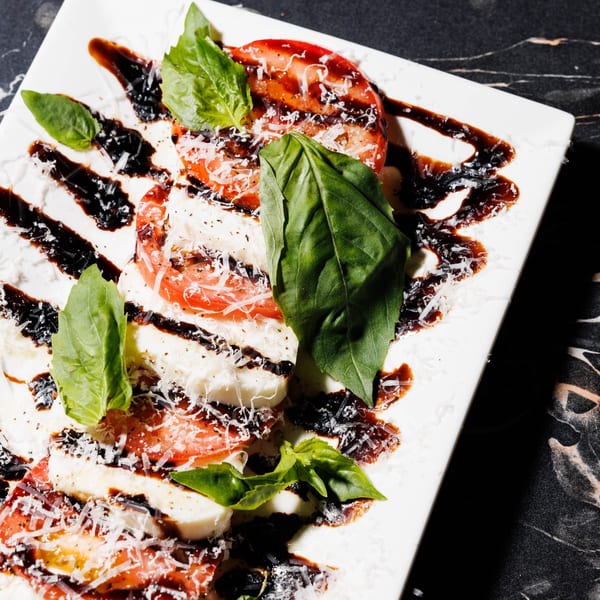 Caprese salad with sliced tomatoes, mozzarella, fresh basil, balsamic glaze, and grated cheese.