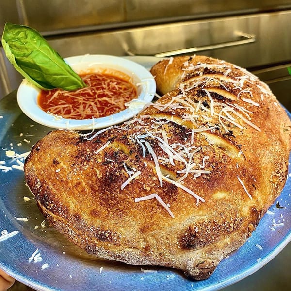 A golden-brown calzone topped with grated cheese and a side of marinara sauce with basil.