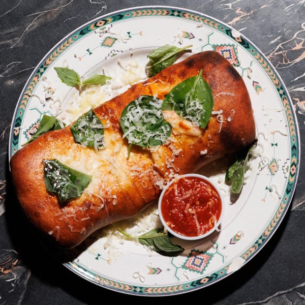 Golden-brown calzone topped with melted cheese, fresh basil, and grated parmesan, served with marinara sauce.