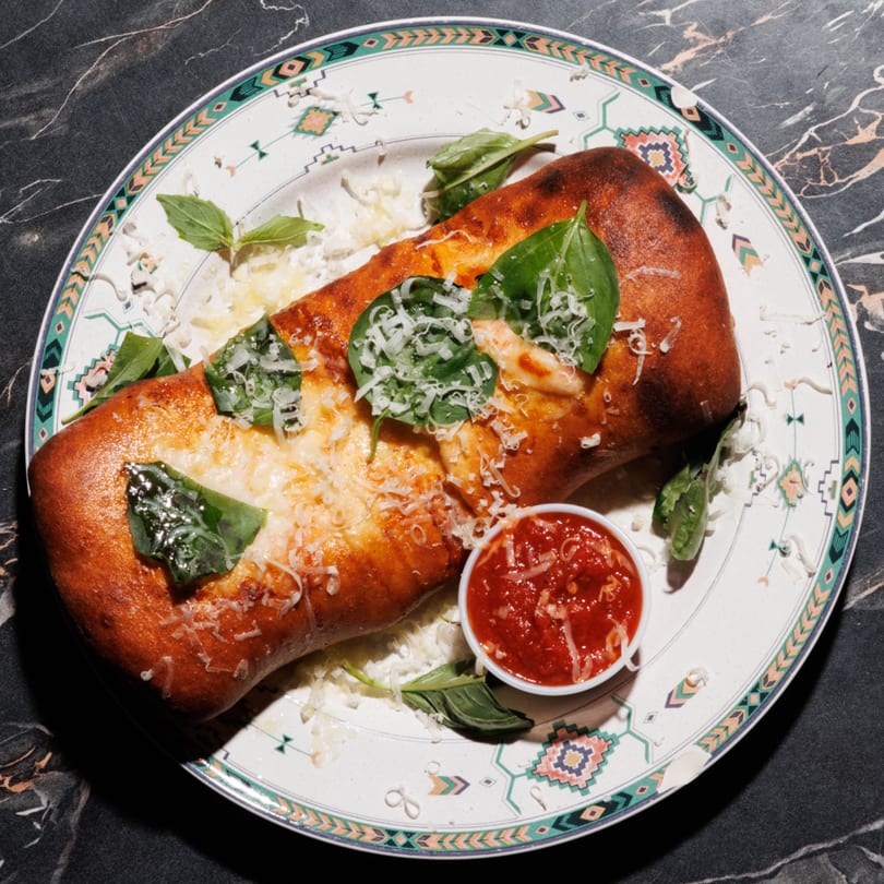 Golden-brown calzone topped with melted cheese, fresh basil, and grated parmesan, served with marinara sauce.