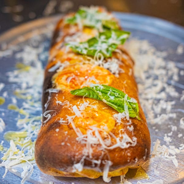 A golden-brown calzone from The Last Round Tavern, topped with melted cheese and fresh basil.