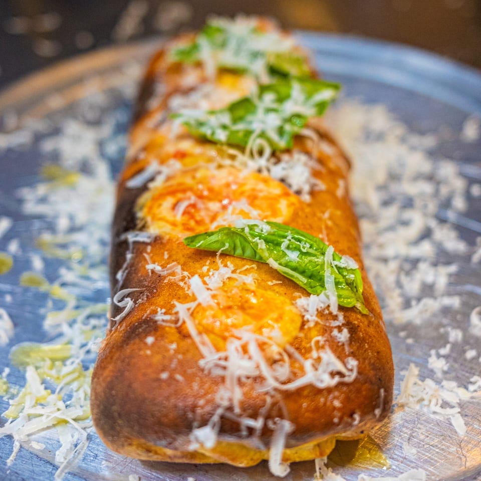 A golden-brown calzone from The Last Round Tavern, topped with melted cheese and fresh basil.